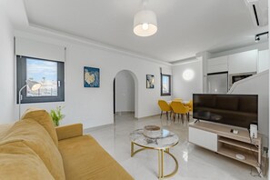 Un salon moderne avec un canapé, une table basse, un téléviseur et un coin repas avec des chaises jaunes.