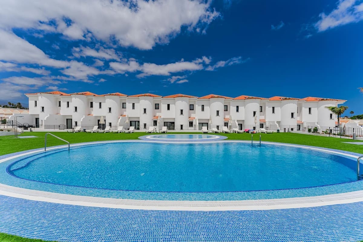 Une piscine bordée de carreaux, entourée de bâtiments blancs aux toits rouges, et un ciel bleu azur.