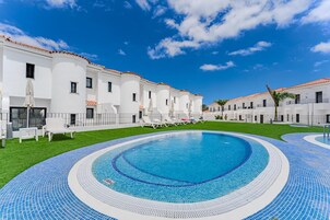 Una piscina al aire libre, sombrillas, sillones reclinables de piscina
