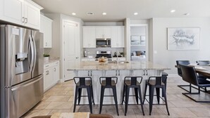 A modern kitchen with white cabinets, stainless steel appliances, a central island with bar stools, and a dining area with a table and chairs. - Game loft, Nerf Wars, Resort Pool, Lazy River & Waterslide • Near Zion (Washington)