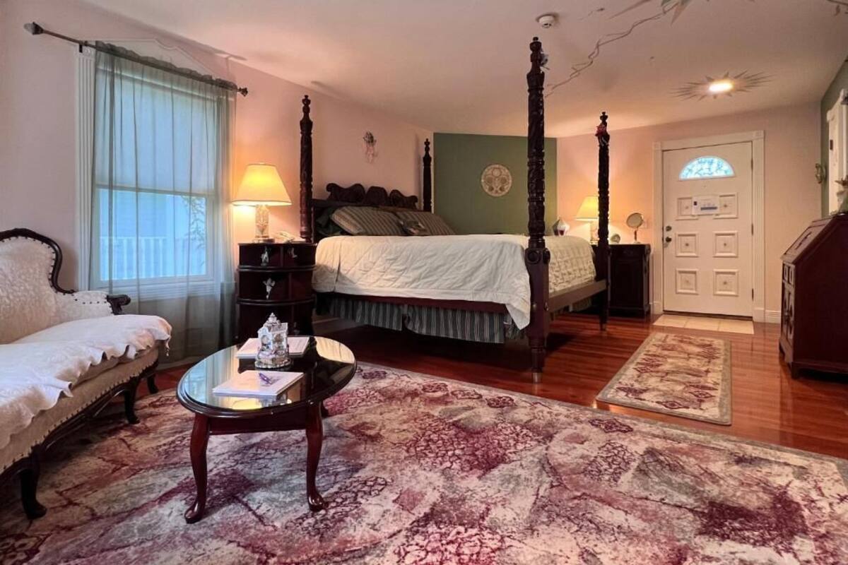 A bedroom with a four-poster bed, a sitting area with a sofa, a glass coffee table, and a large patterned rug.