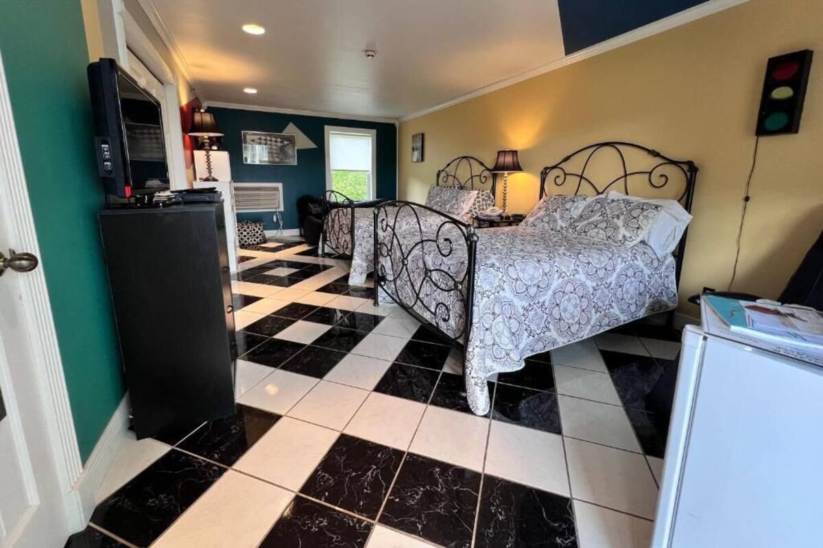 A bedroom with a checkered floor, a bed with patterned bedding, a desk with a television, and a window with blinds.