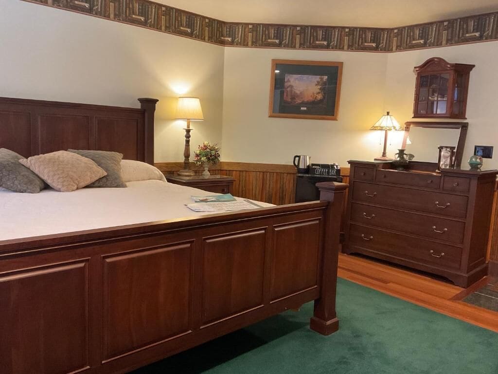 Ein Schlafzimmer mit einem hölzernen Bett, zwei Nachttischen mit Lampen, einer Kommode und einem gerahmten Bild an der Wand.