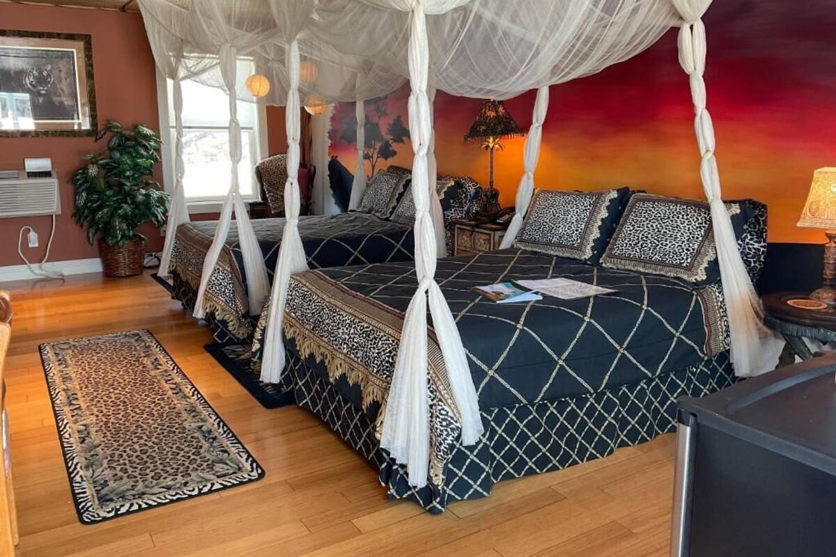 A bedroom with a canopy bed, a leopard print rug, and a sunset mural.