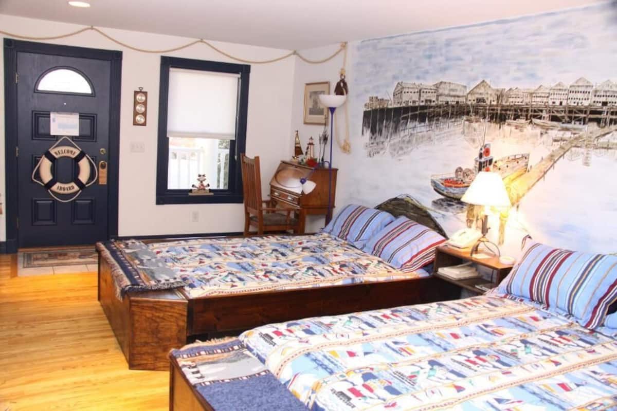 A bedroom with two wooden beds, a large window, a door with a welcome sign, and a mural of a coastal scene.