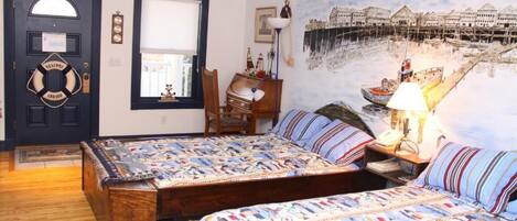 A bedroom with two wooden beds, a large window, a door with a welcome sign, and a mural of a coastal scene.