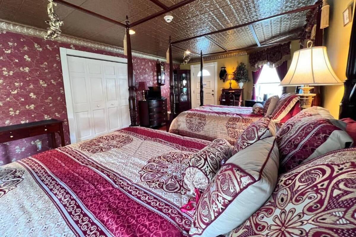 A room with two beds, a wooden ceiling, a white door, and a lamp.