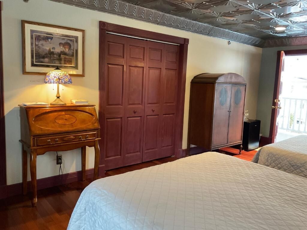 Une chambre à coucher avec un lit, une commode en bois, une grande armoire et un tableau encadré au mur.