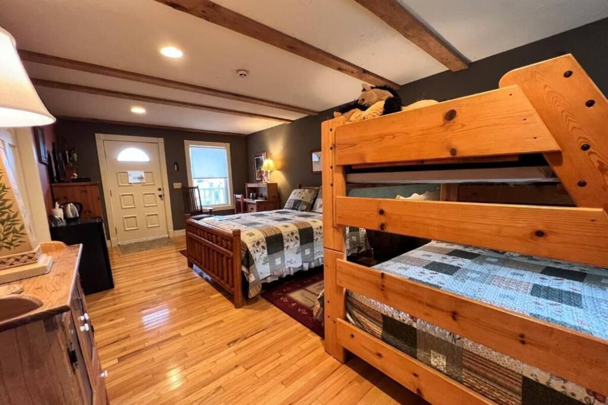 A bedroom with two wooden bunk beds, a wooden dresser, a desk, and a lamp.