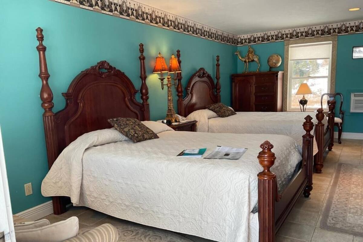 A bedroom with two beds, a nightstand, a lamp, a dresser, and a window.