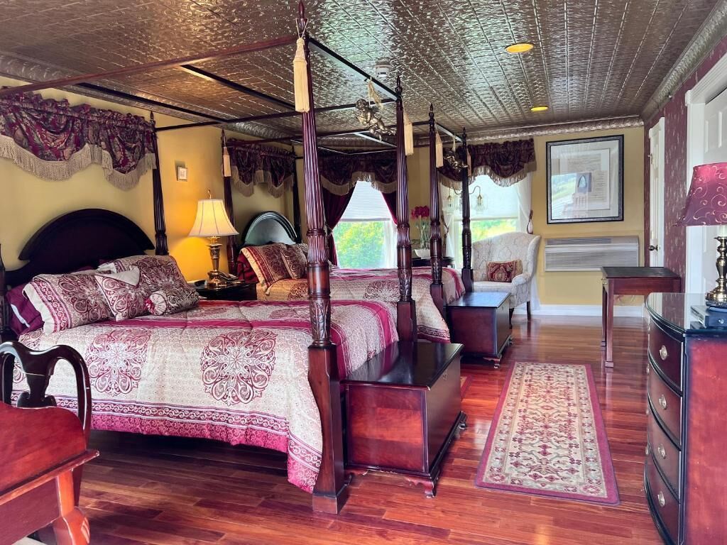 A four-poster bed with a canopy, a wooden dresser, a nightstand, and a desk with a lamp.