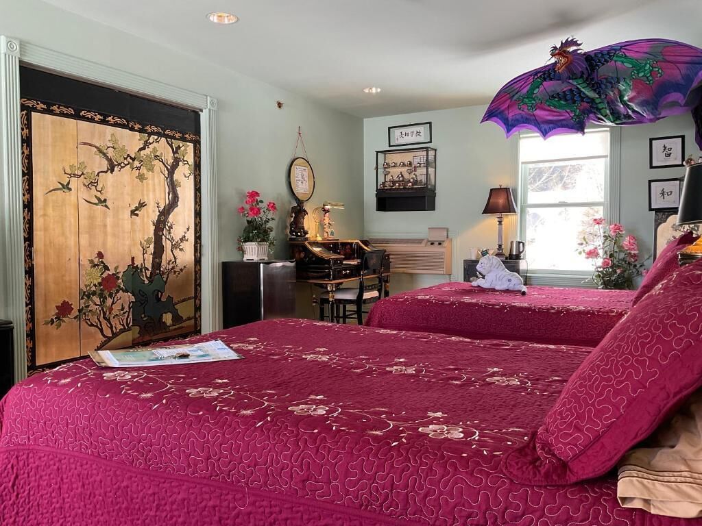 Ein Schlafzimmer mit zwei Betten, einem Schreibtisch, einem Stuhl, einem Klavier und einer Dekoration mit einem Drachen.