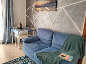 A living room with a blue sofa, a dining table with chairs, a painting on the wall, and a patterned rug. - Mery Giò vacation home in San Pietro in Bevagna suitable for families and groups (San Pietro In Bevagna)