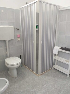 Een badkamer met toilet, douchecabine en een plankunit.
