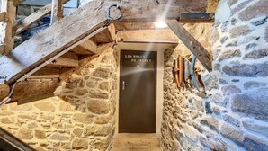 Ein Zimmer mit Stehwänden, einer Holztreppe, einer Tür mit der Aufschrift 'LES HEAUX DE BREITAT' und einer rustikalen Holzbalkendecke.