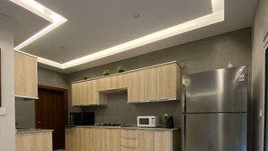 A modern kitchen with wooden cabinets, a stainless steel refrigerator, a microwave, and a gas stove. - Lemon Beach Chalet in Durrat Al Arous (درة العروس)