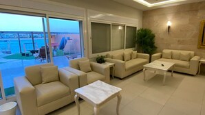 A modern living room with a large sliding glass door leading to a balcony, beige sofas, a white coffee table, and a potted plant. - Lemon Beach Chalet in Durrat Al Arous (درة العروس)