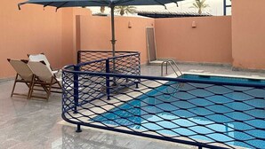 A swimming pool with a blue net, two lounge chairs, and a blue umbrella. - Lemon Beach Chalet in Durrat Al Arous (درة العروس)