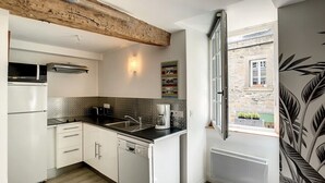 A kitchen with white cabinets, a black countertop, a coffee maker, and a window with a view of a stone building. - "Roches Douvres": Apartment in old Paimpol (Paimpol)