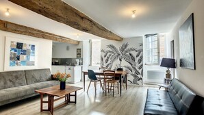 A modern living room with a wooden ceiling, a sofa, a dining table with chairs, a black leather couch, and a large window. - "Roches Douvres": Apartment in old Paimpol (Paimpol)