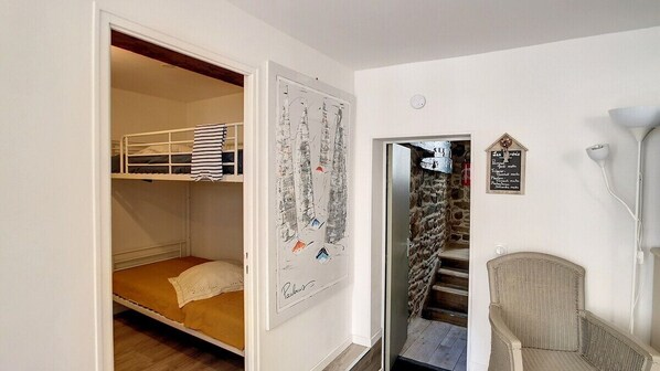 Una habitación con una cama litera, un cuadro enmarcado, una silla y una escalera.