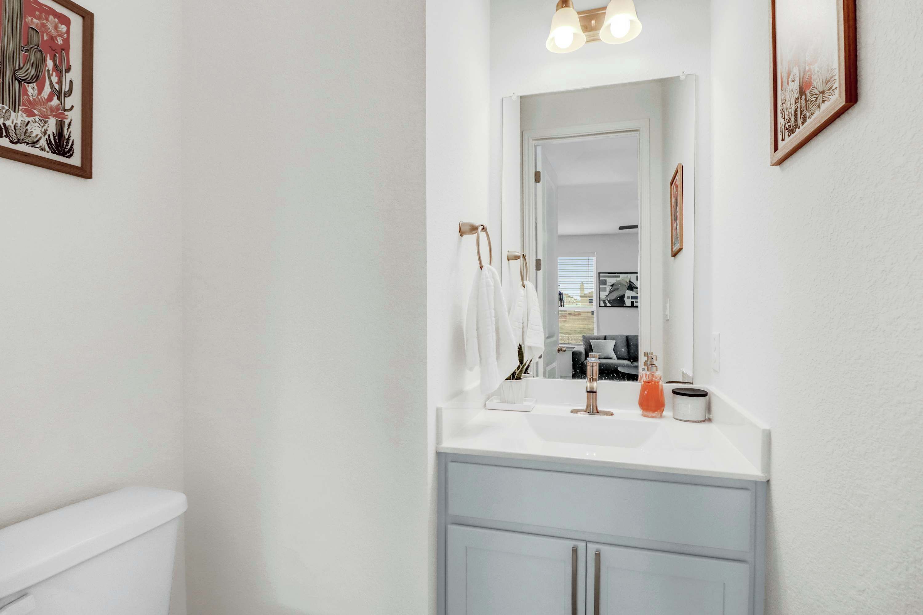 Un baño con inodoro blanco, lavamanos con espejo y una lámpara sobre el espejo.