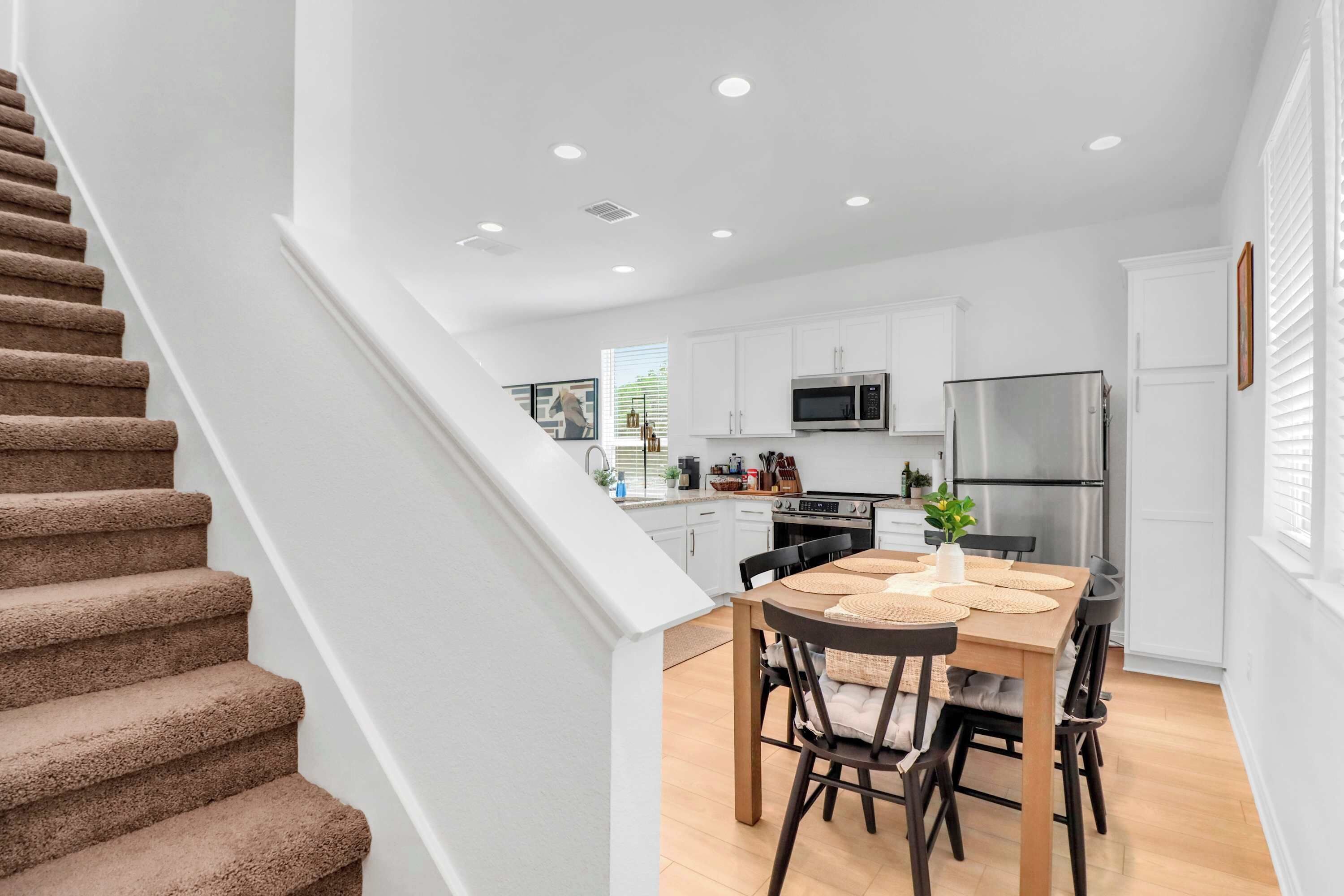A modern kitchen with white cabinets, a stainless steel refrigerator, and a dining area with a wooden table and chairs.