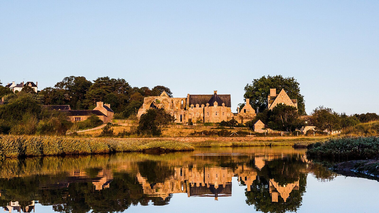 Un complesso di edifici storici con un fossato che riflette l'architettura e la vegetazione.