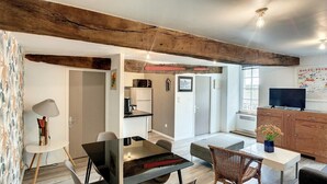 A modern kitchen with white cabinets, a microwave, and a refrigerator. There is a dining area with a table and chairs, and a television in the corner. - "Rosedo": Charming apartment in old Paimpol (Paimpol)