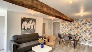 A living room with a sofa, a dining table with chairs, a vase with flowers, and a wall with a leaf pattern. - "Rosedo": Charming apartment in old Paimpol (Paimpol)