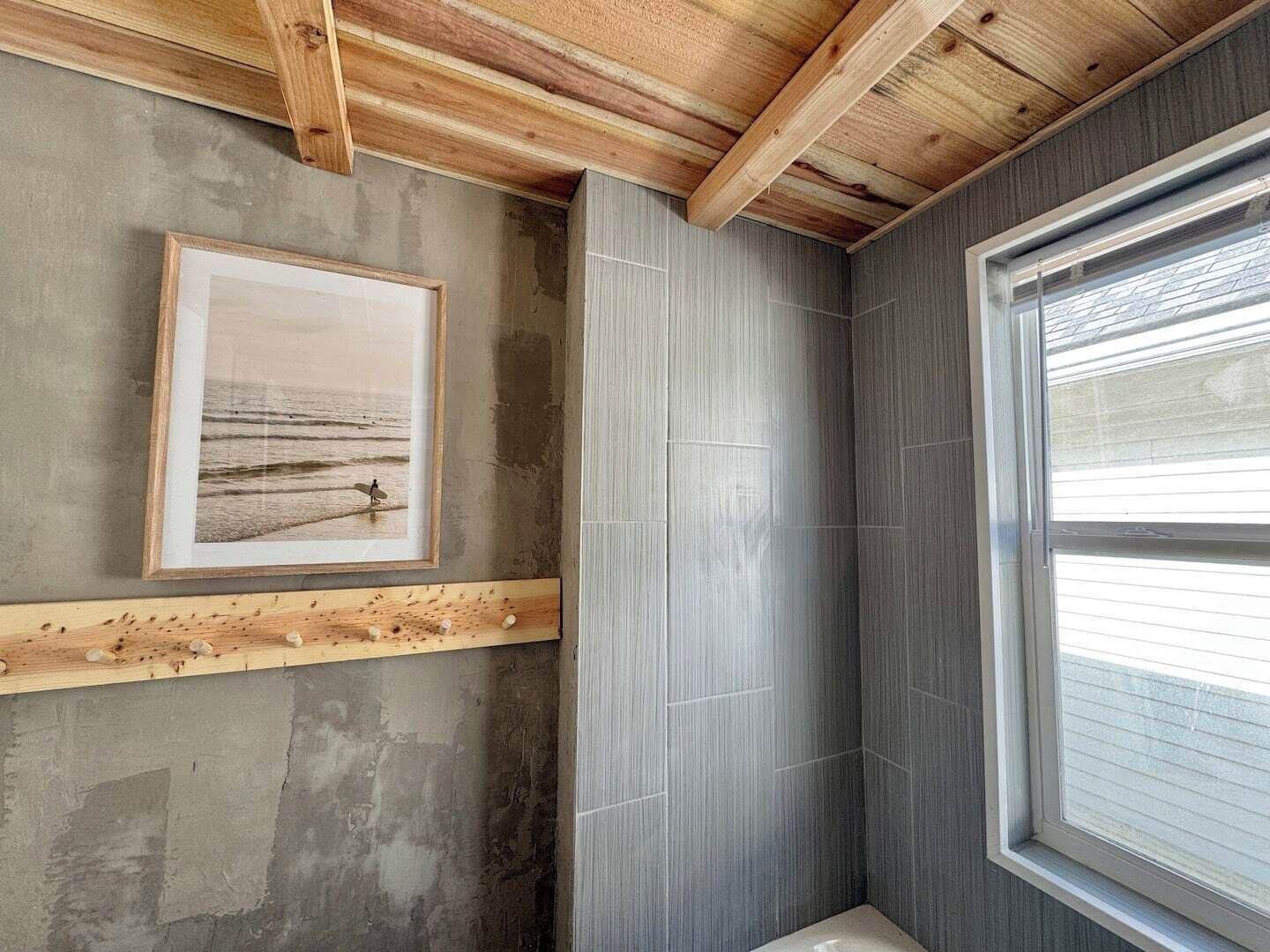 A room with a framed picture on the wall, a wooden beam ceiling, and a window with blinds.