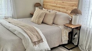 Cama bem arrumada com cabeceira de madeira, duas luminárias de apoio e mesa de cabeceira com abajur.