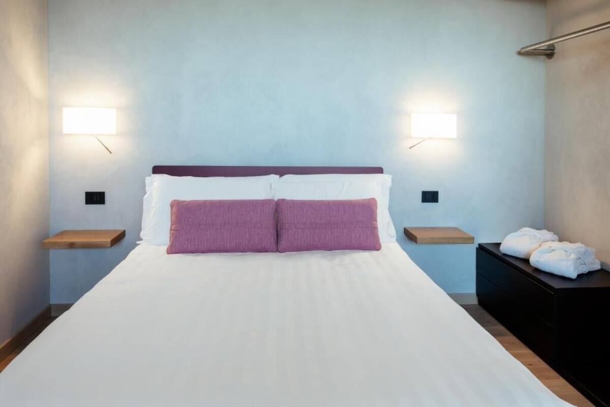 A hotel room with a bed, two bedside tables, a nightstand, and a black dresser with towels.