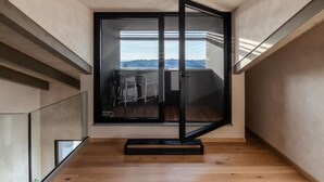 A modern loft bedroom with a large sliding glass door leading to a balcony, wooden flooring, and a minimalist design. - Vineho (Barolo)