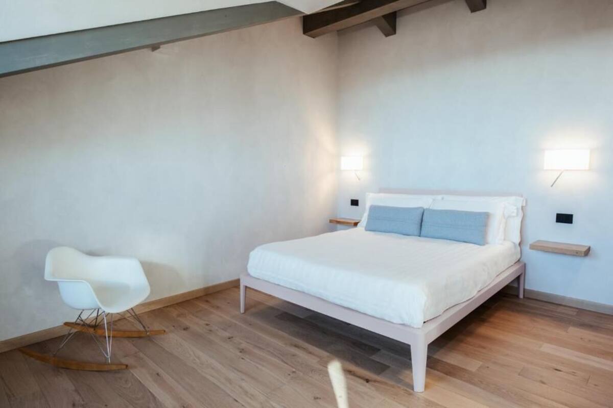 A bedroom with a bed, a rocking chair, and two wall-mounted lights.