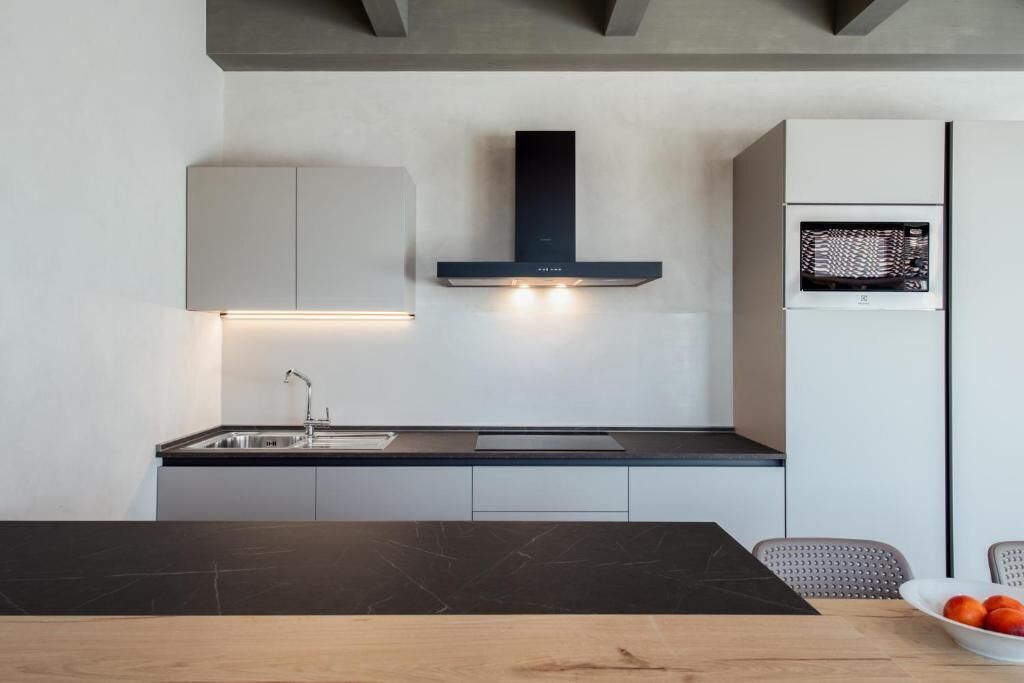 Uma cozinha moderna com bancada preta, pia de aço inoxidável e micro-ondas embutido.