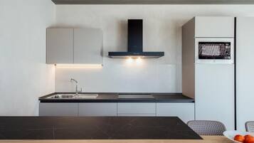 Uma cozinha moderna com bancada preta, pia de aço inoxidável e micro-ondas embutido.