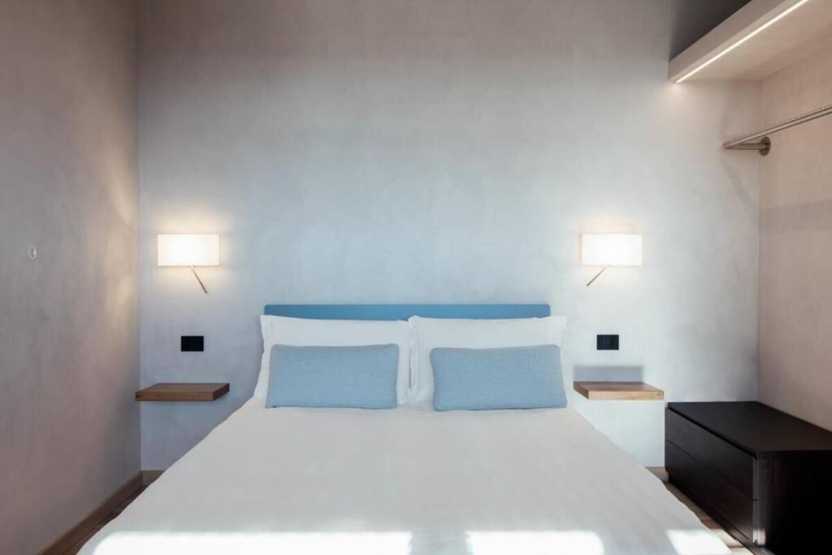A modern hotel room with a large bed, bedside tables, and wall-mounted lights.