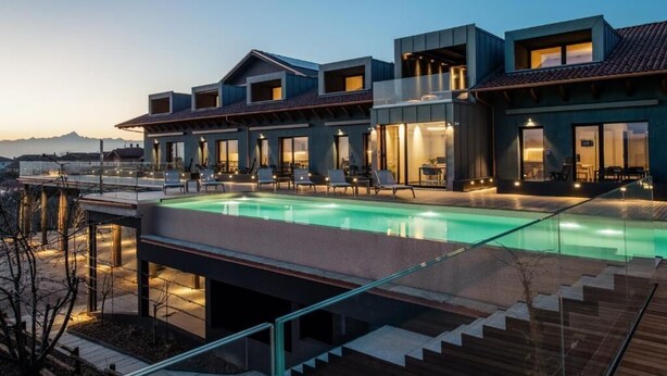 A modern hotel with a swimming pool, outdoor seating, and a view of the mountains. - Vineho (Barolo)