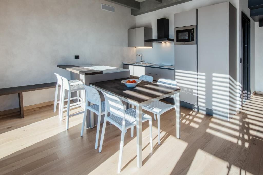 Una cocina moderna con armarios blancos, microondas integrado y comedor con mesa de madera y sillas blancas.