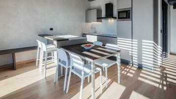 Una cocina moderna con armarios blancos, microondas integrado y comedor con mesa de madera y sillas blancas.