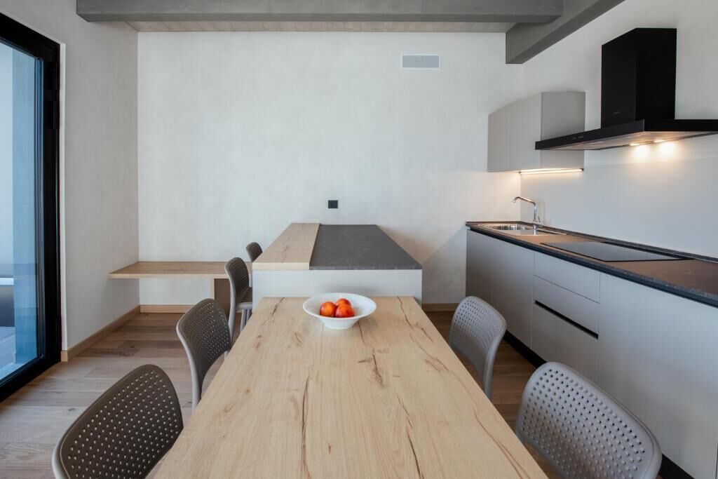 A modern kitchen with a dining table, chairs, and a bowl of fruit.
