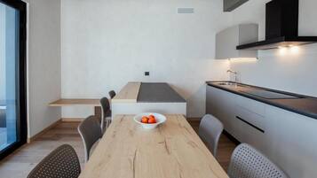 A modern kitchen with a dining table, chairs, and a bowl of fruit.