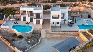 En moderne villa med swimmingpool, udendørs møbler og en støttemur af sten.