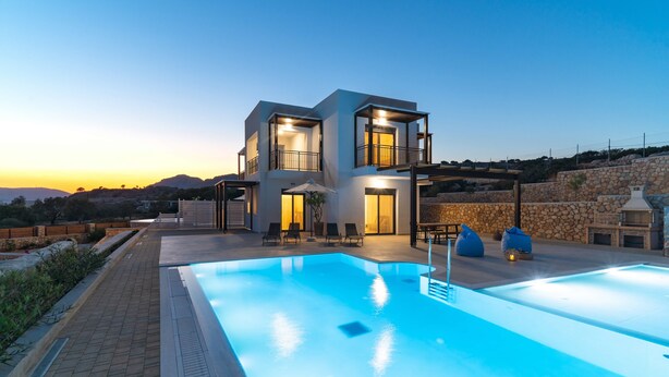 Et moderne hus med to etager, swimmingpool, udendørs møbler og en stenvæg.