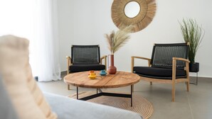 En moderne stue med et rundt træbord, to sorte fletstole, et rundt spejl og en potteplante.