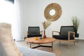 Ein modernes Wohnzimmer mit einem runden Couchtisch aus Holz, zwei schwarzen Korbstühlen, einem runden Spiegel und einem Topfpflanzen.