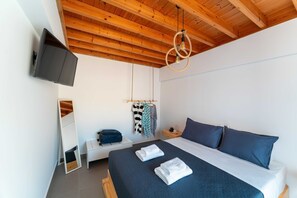 Ein Schlafzimmer mit einem Bett, einem Fernseher, einer Hängelampe, einer Bank und einem Kleiderständer mit Kleidung.