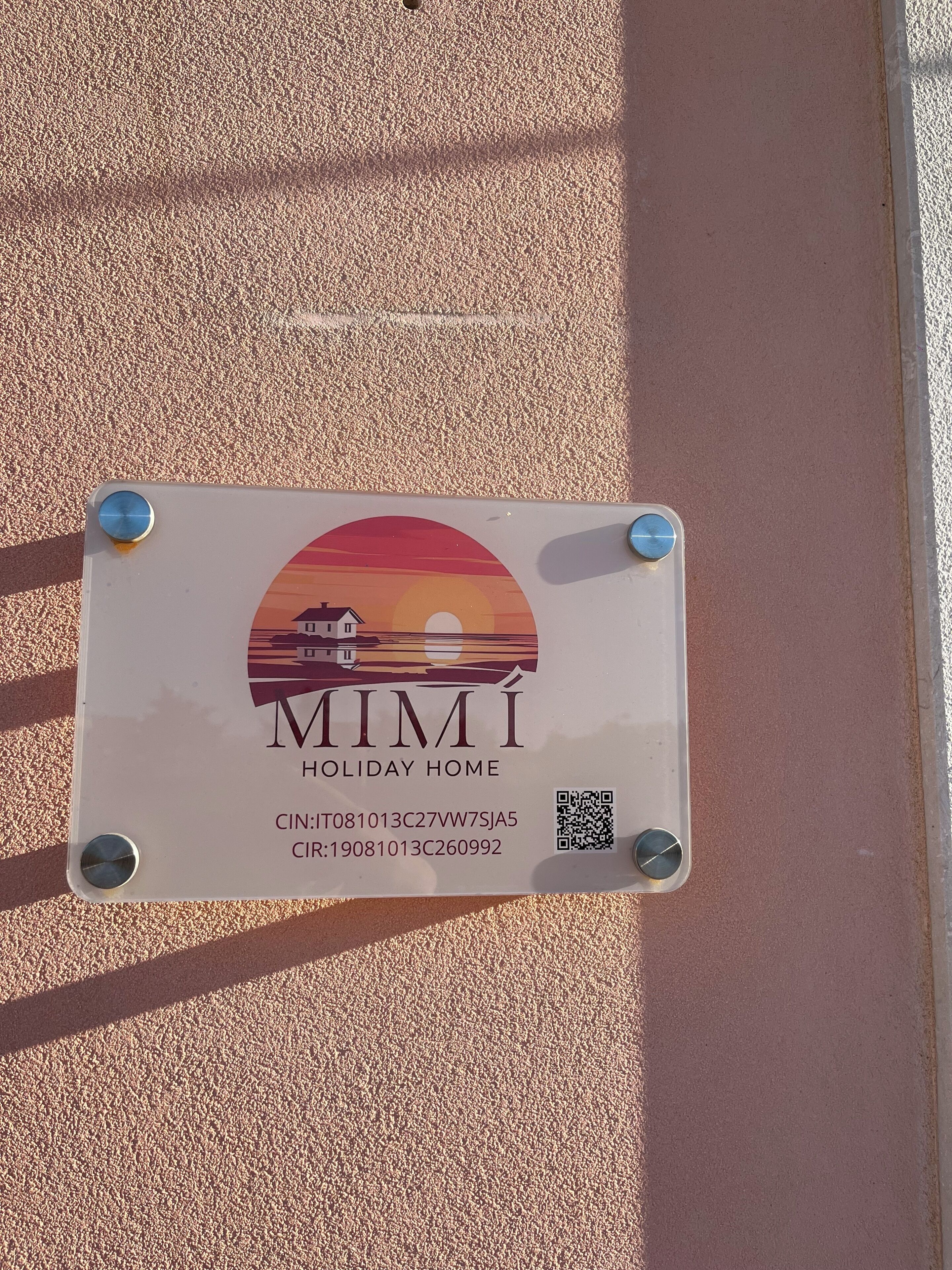 A sign with a sunset illustration, 'MIMI HOLIDAY HOME' text, and two QR codes.