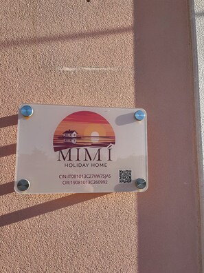 Un panneau illustré d’un coucher de soleil, avec l’inscription « MIMI HOLIDAY HOME » et deux codes QR.